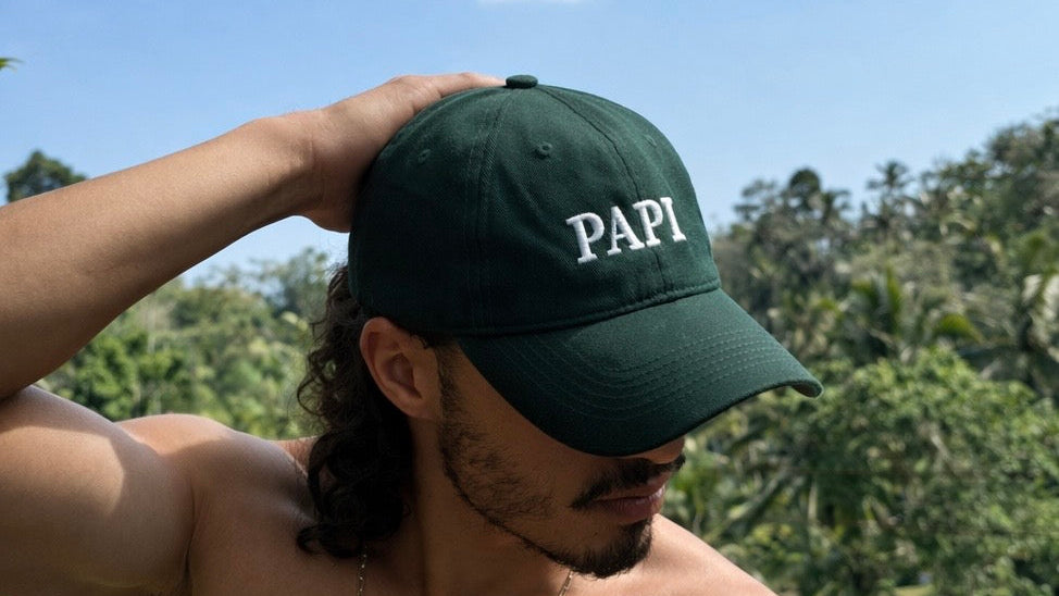 Man wearing a green cap with 'PAPI' text outdoors against a blue sky and trees.