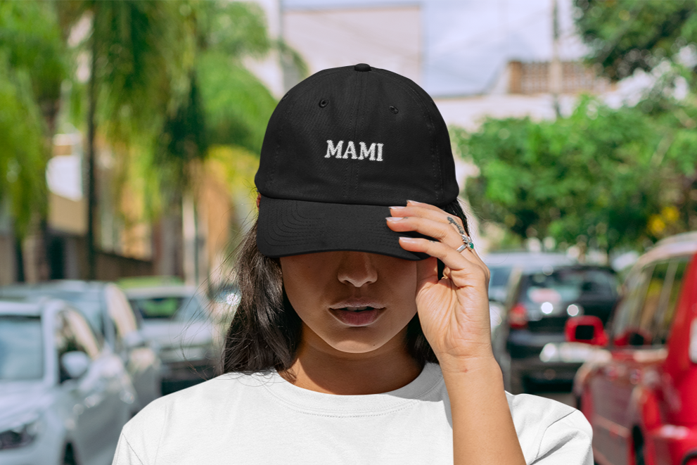 A person wearing a black cap with the text 'MAMI' on it, set against a tropical landscape.
