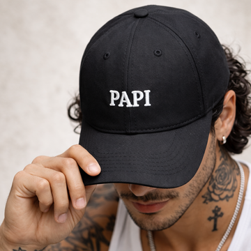 Man wearing a black cap with 'PAPI' text, tattoos visible on arms and neck, white tank top.